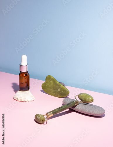 Cosmetic product in a glass bottle with a pipette and gua sha e scraper and roller. Smooth stones nearby. The concept of skin care, cosmetology.