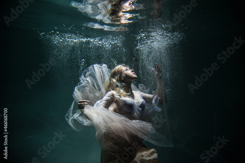 Girl in a white dress underwater around a lot of bubbles on a dark background