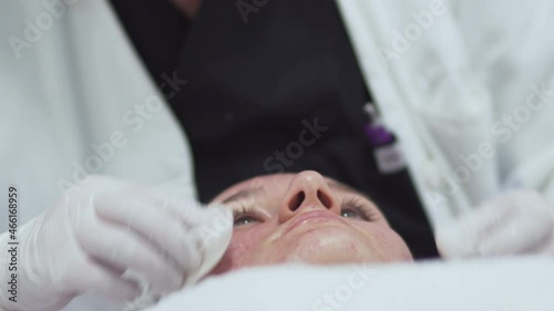 Beautician applying moisturising vitaminic gel on teen girl's problematic acne skin in spa salon, close up photo