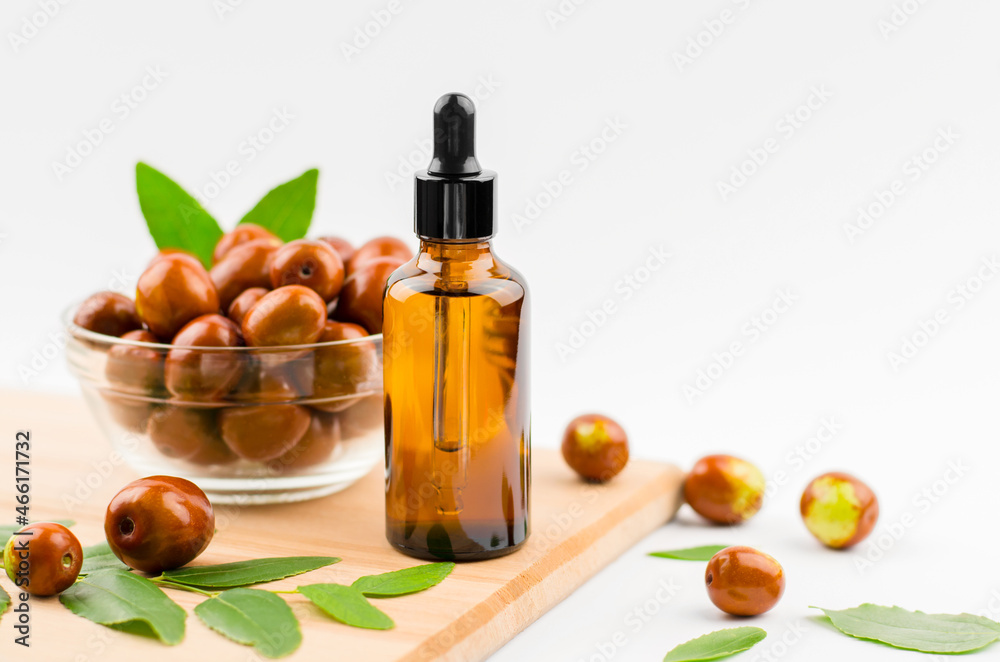 Jojoba oil in a bottle with a dropper on a wooden table with ripe jojoba fruits. Chinese Date Oil and Fruit Jojoba oil in a bottle with a dropper on a wooden table with ripe jojoba fruits. Chinese Date Oil and Fruit