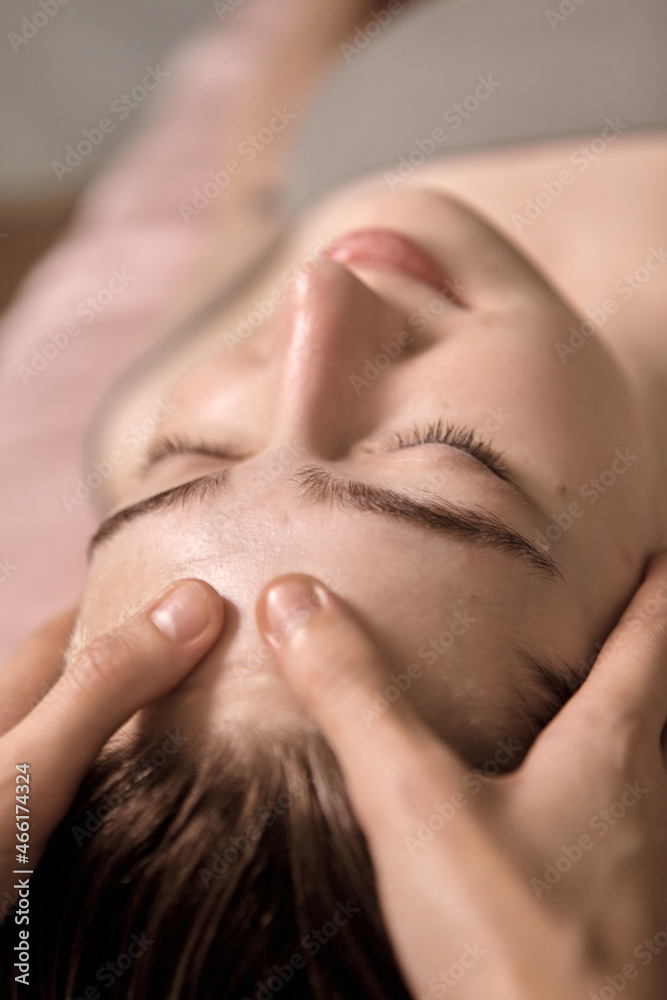 Young beautiful woman is getting a relaxing head and face massage in wellness center. Masseur doing massage the head of an young beautiful girl woman in the spa salon close up macro Young beautiful woman is getting a relaxing head and face massage in wellness center. Masseur doing massage the head of an young beautiful girl woman in the spa salon close up macro