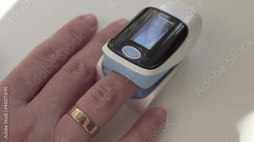 Close up of digital pulse oximeter on woman's finger, medical monitoring device blinking and showing oxygen saturation level on display.