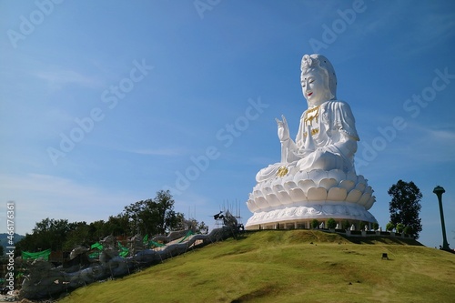 Huge white Buddha statue sits on top of a hill