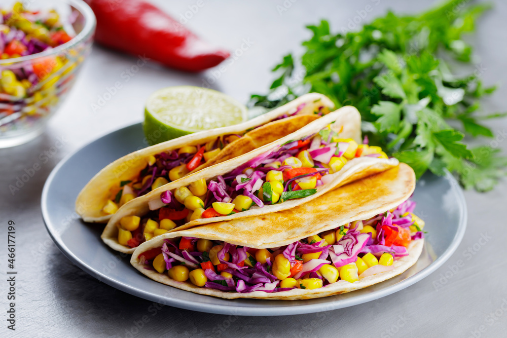 Vegan tacos with corn, purple cabbage and tomatoes on a gray plate. Mexican tacos with vegetables and guacamole on gray background. Close-up