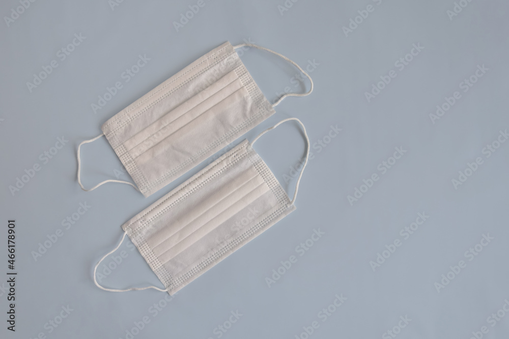 Two white medical masks on light blue background. Virus protection remedies. Top view. Close-up. Selective focus. Two white medical masks on light blue background. Virus protection remedies. Top view. Close-up. Selective focus.