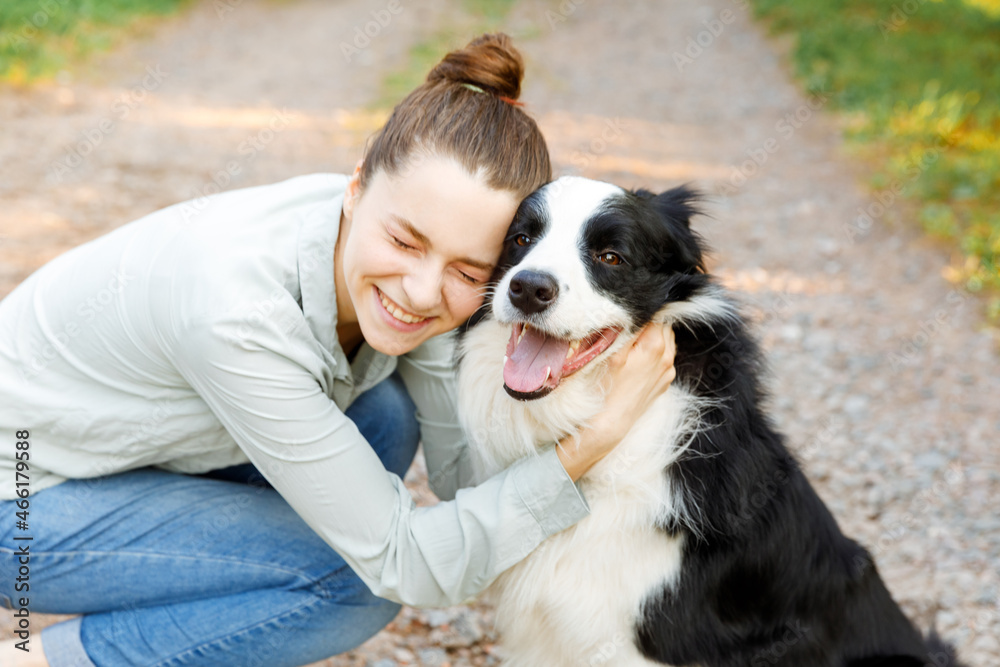 Smiling young attractive woman playing with cute puppy dog border collie on summer outdoor background. Girl holding embracing hugging dog friend. Pet care and animals concept