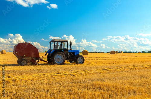 A tractor uses trailed bale machine to collect straw in the field and make round large bales. Agricultural work  baling  baler  hay collection in the summer field.