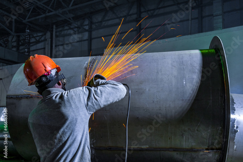 Weld stripping after assembly and welding of stainless steel pipe. The worker does the work with an angle grinder. Spray of sparks.