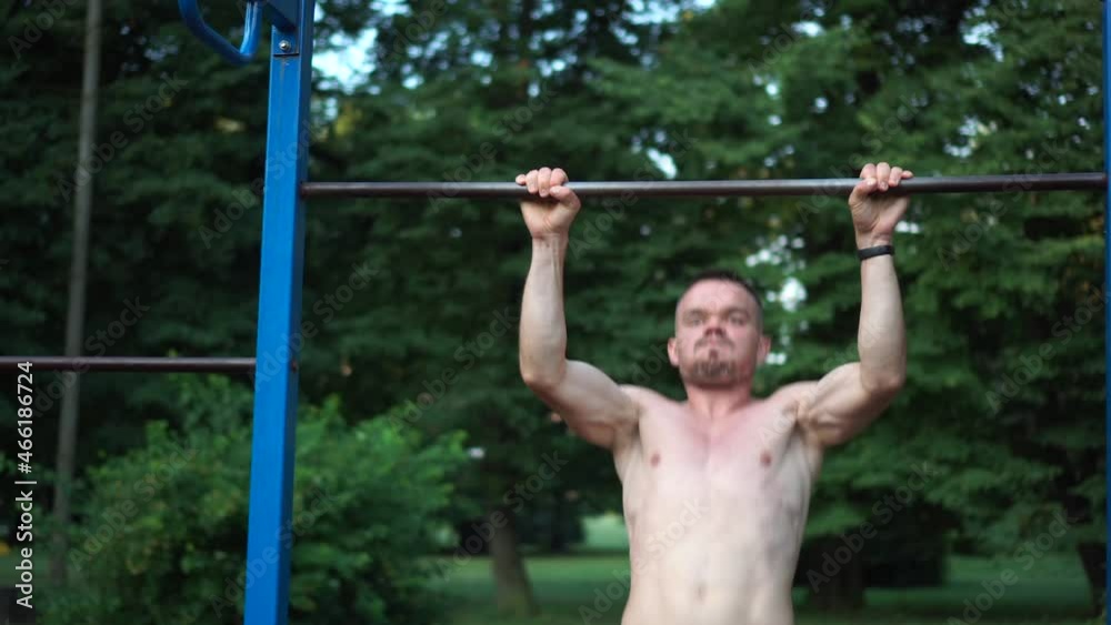 Man makes pull-ups on turnstile. Athletic guy pulls himself up on horizontal bar. Sport activities in fresh air. Healthy lifestyle Man makes pull-ups on turnstile. Athletic guy pulls himself up on horizontal bar. Sport activities in fresh air. Healthy lifestyle