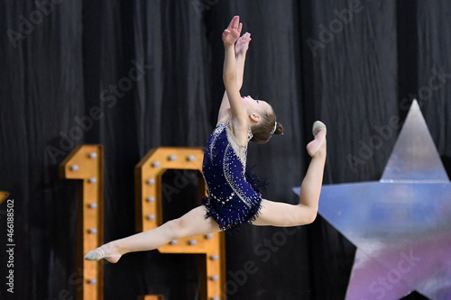 A girl dressed as a gymnast demonstrates her sports skills on the playground. The gymnast athlete performs acrobatic elements. Rhythmic gymnastics competition