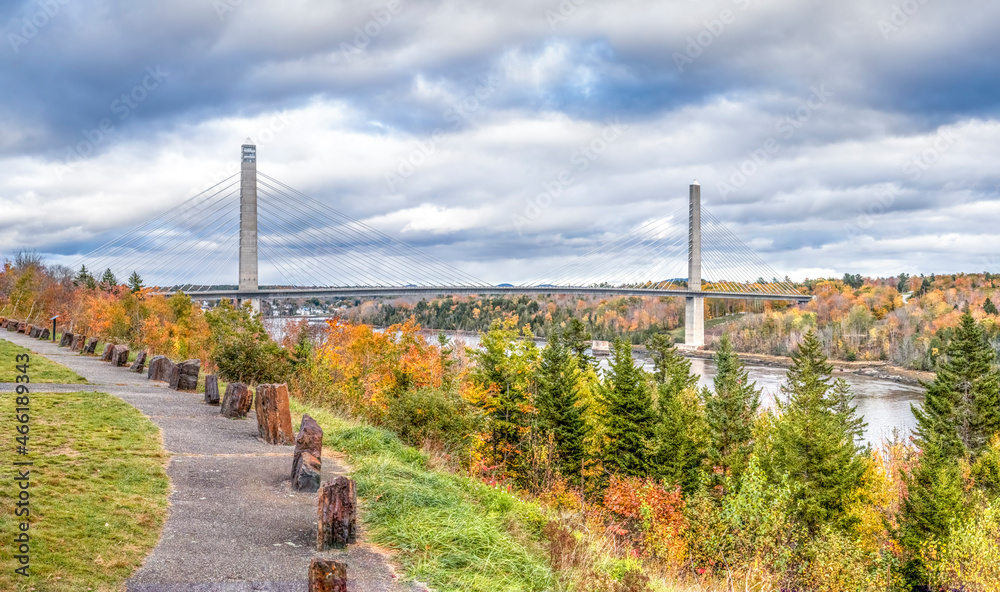 The Penobscot Narrows Bridge spans the Penobscot River near Bucksport, Maine surrounded by colorful fall foliage on a cloudy autumn day.