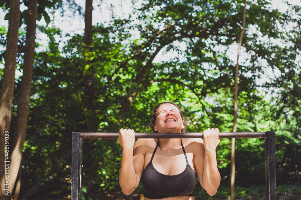 Woman doing iron bar exercises outdoors. Caucasian girl exercising on free gym equipment in park. Photo with space for text.