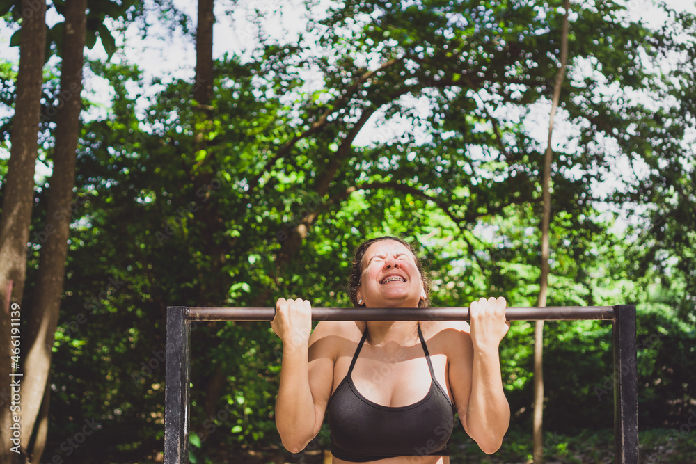 Woman doing iron bar exercises outdoors. Caucasian girl exercising on free gym equipment in park. Photo with space for text. Woman doing iron bar exercises outdoors. Caucasian girl exercising on free gym equipment in park. Photo with space for text.