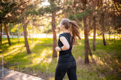 Back view a girl in a black sports uniform is jogging in the evening park. Self-sports concept. 