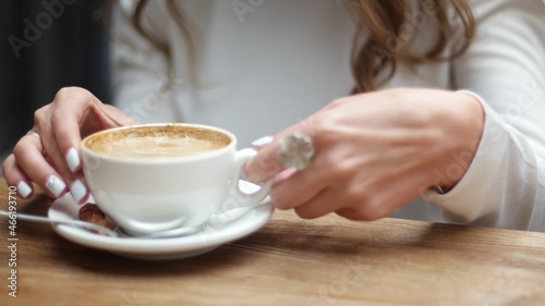 Side view of women hands with white cup of black coffe on light wooden table background. Media. Closeup shot of delicate girls hands taking small cup of coffee.