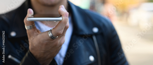 Cropped view of smartphone in hand of man recording voice message outdoors, banner 