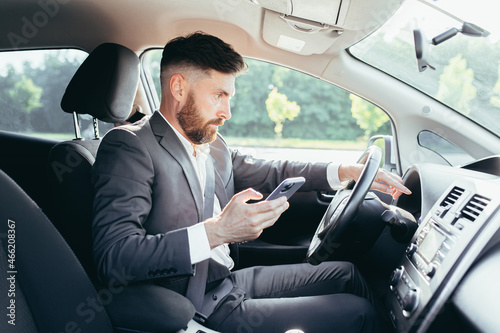 Male businessman sitting behind the wheel of a car, frustrated can not understand the steering and instructions funky car, reads additional information from the phone © Liubomir