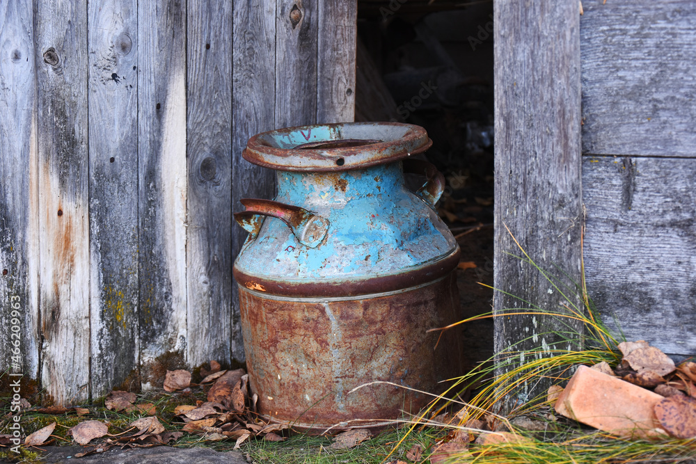 An image of a rusted old vintage milk can in the doorway of an old rundown barn. 