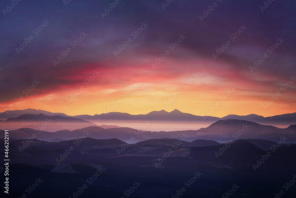 Mountains in fog at sunset. Dramatic landscape with cloudy sky, valley, mist, mountains and bright sunshine under mountain tops.