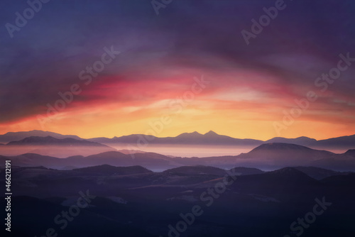 Mountains in fog at sunset. Dramatic landscape with cloudy sky, valley, mist, mountains and bright sunshine under mountain tops.