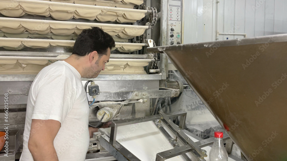 Pending baker on his factory's bread-making machines. Baker making bread in his small business machines. Concept bread, baker, factory, business, bakery, artisan. Pending baker on his factory's bread-making machines. Baker making bread in his small business machines. Concept bread, baker, factory, business, bakery, artisan.