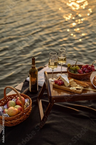 Amazing sunset on the lake, white wine, fruit cake, apples, grapes, brie cheese, biscuits. Autumn aesthetic picnic.