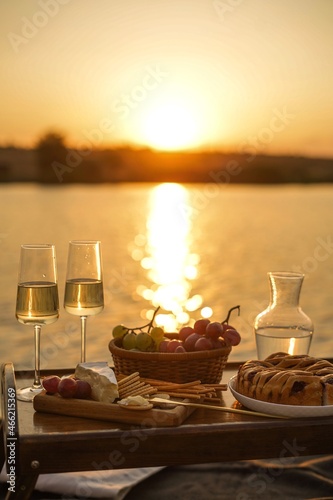 Amazing sunset on the lake, white wine, fruit cake, apples, grapes, brie cheese, biscuits. Autumn aesthetic picnic.