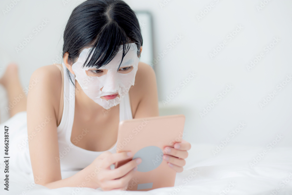 Beautiful young asian woman with sheet facial mask lying watching tablet computer on bed at bedroom, beauty girl applying face mask for skincare of wrinkle at home, skin care, health and wellness. Beautiful young asian woman with sheet facial mask lying watching tablet computer on bed at bedroom, beauty girl applying face mask for skincare of wrinkle at home, skin care, health and wellness.