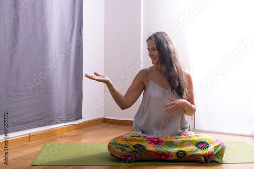 woman practicing yoga or meditation in her living room sitting on a mat on the floor