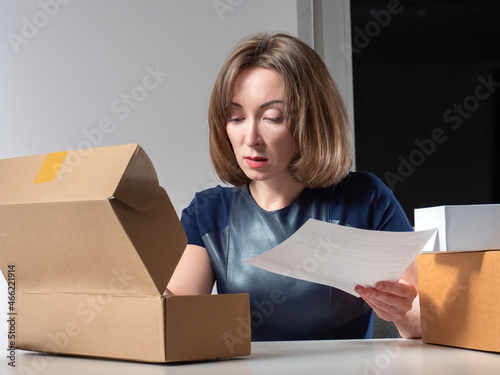 Woman unpacks a cardboard box. Concept - girl unpacks Internet order. She looks into open box. Office worker received package. Unpacking a parcel from online store. Unpacking boxes. photo