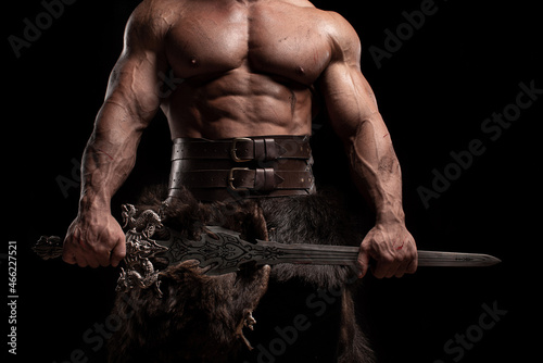 Close up muscular ancient warrior barbarian with fantasy sword on black background