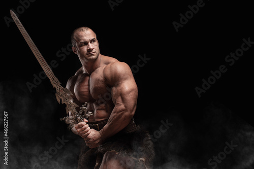 Ferocious muscular ancient warrior barbarian with fantasy sword on black background photo