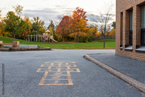School building and schoolyard with playground for children in evening in fall season. Selective focus on hopscotch. Back to school educational concept. photo