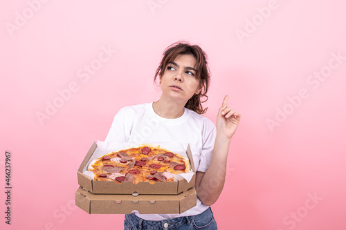 Pensive attractive girl with pizza in a box on a pink background  copy space.