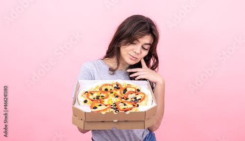 Attractive girl with pizza in a box for delivery on a pink background.