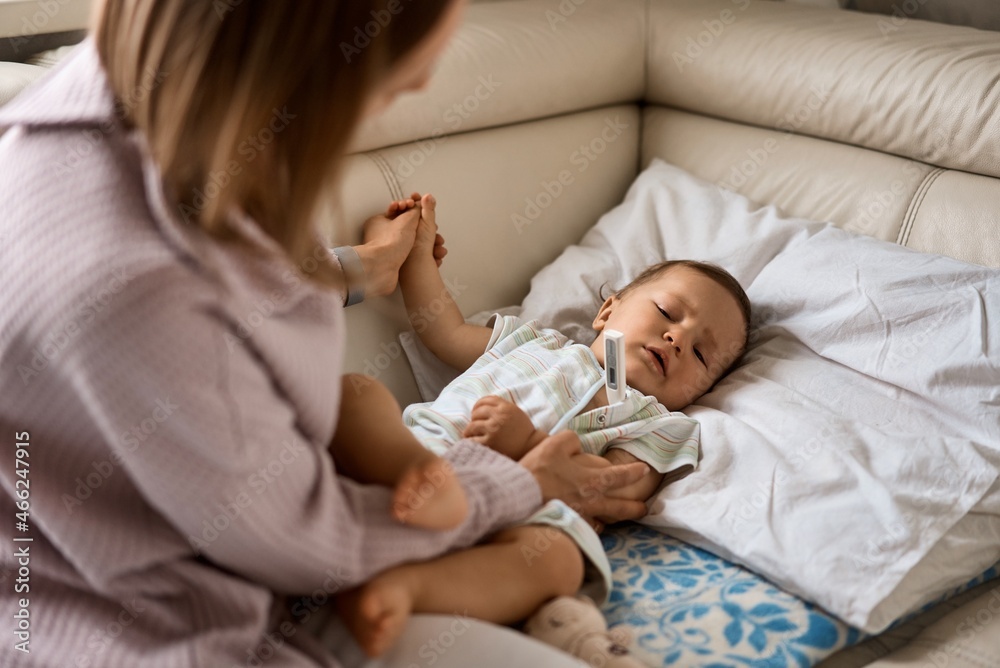 Mother measuring temperature of her ill kid at background. Sick child with high fever lying at sofa at home. High quality 4k footage Mother measuring temperature of her ill kid at background. Sick child with high fever lying at sofa at home. High quality 4k footage