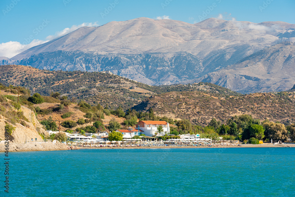 Wind-protected beach and bay with sun loungers and umbrellas in the popular tourist resort of Agia Galini in the south of Crete. In the background the IDA mountain range with the mighty Psiloritis