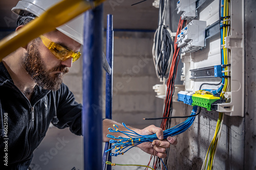 A male electrician works in a switchboard with an electrical connecting cable. photo