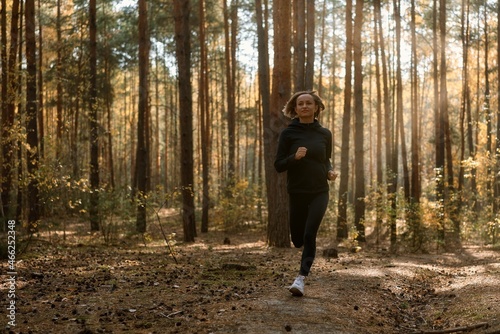 Young athletic woman jogging in forest in sunny morning. Healthy lifestyle concept.