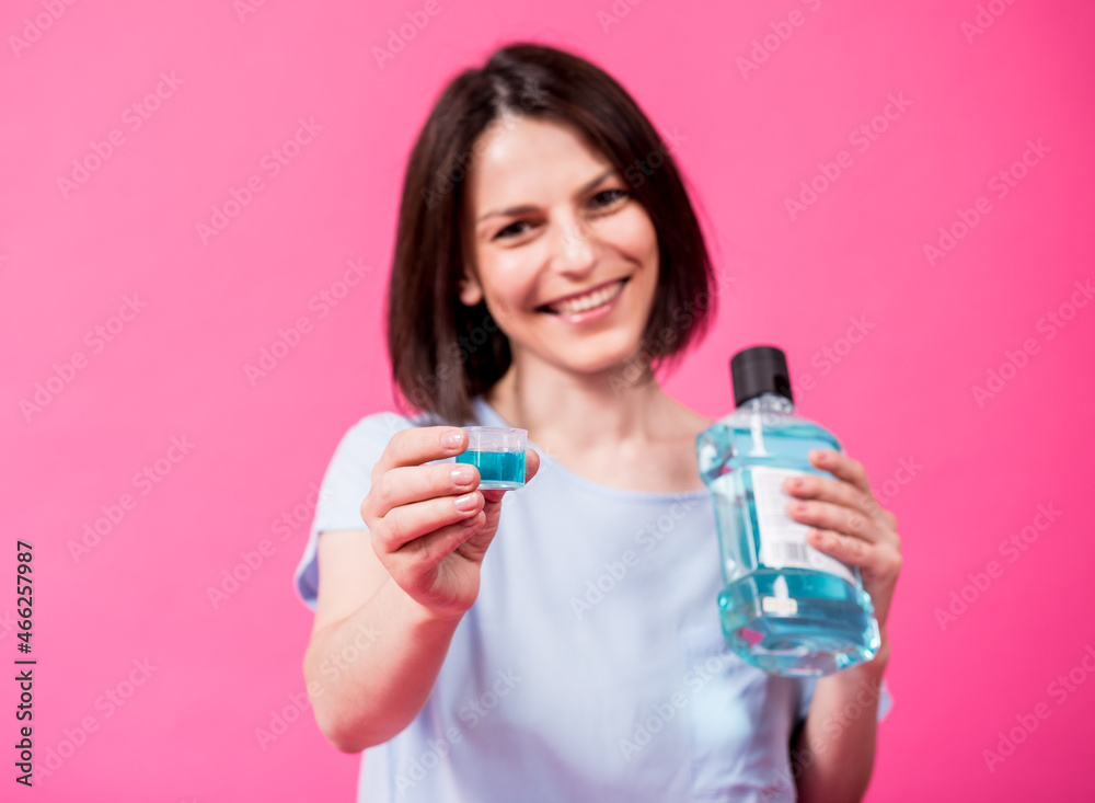 Beautiful girl uses mouthwash on the pink background Beautiful girl uses mouthwash on the pink background
