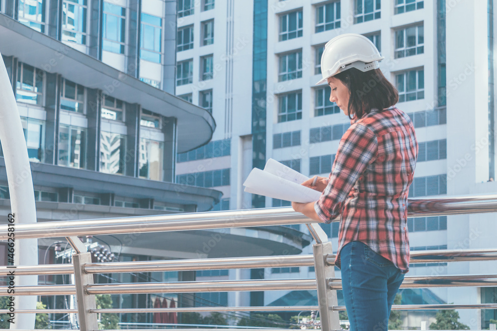 Worker women with white helmet who standing and looking paper plans at construction site.. Worker women with white helmet who standing and looking paper plans at construction site..