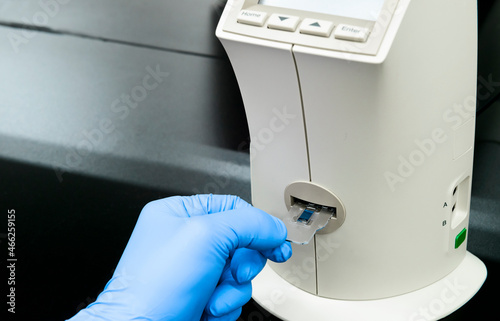 Scientist inserts two-chambered slide containing trypan blu-stained cells into automatic cell counter photo