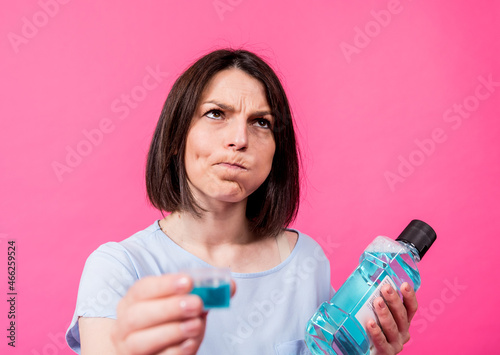 Beautiful girl uses mouthwash on the pink background photo