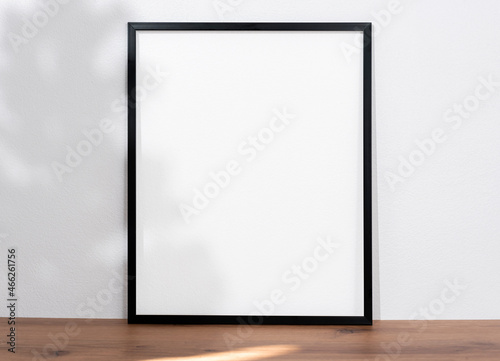 mockup black frame with light and shadow tree on wood table. empty white frame.