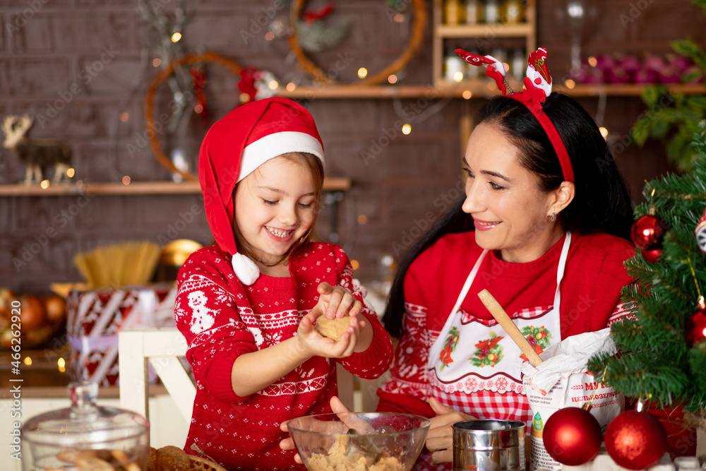 mom and daughter in a dark kitchen with a Christmas tree cook ginger cookies for the New Year or Christmas and smile in a Santa Claus hat