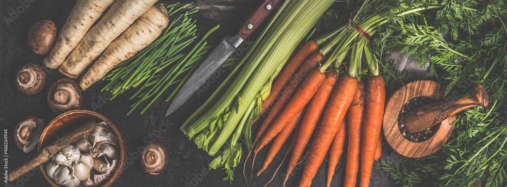 Various vegetables and kitchen utensils on dark rustic kitchen table: Carrots, garlic, mushrooms, celery and parsnip. Healthy lifestyle with vegetarian food. Top view. Banner. - obrazy, fototapety, plakaty 