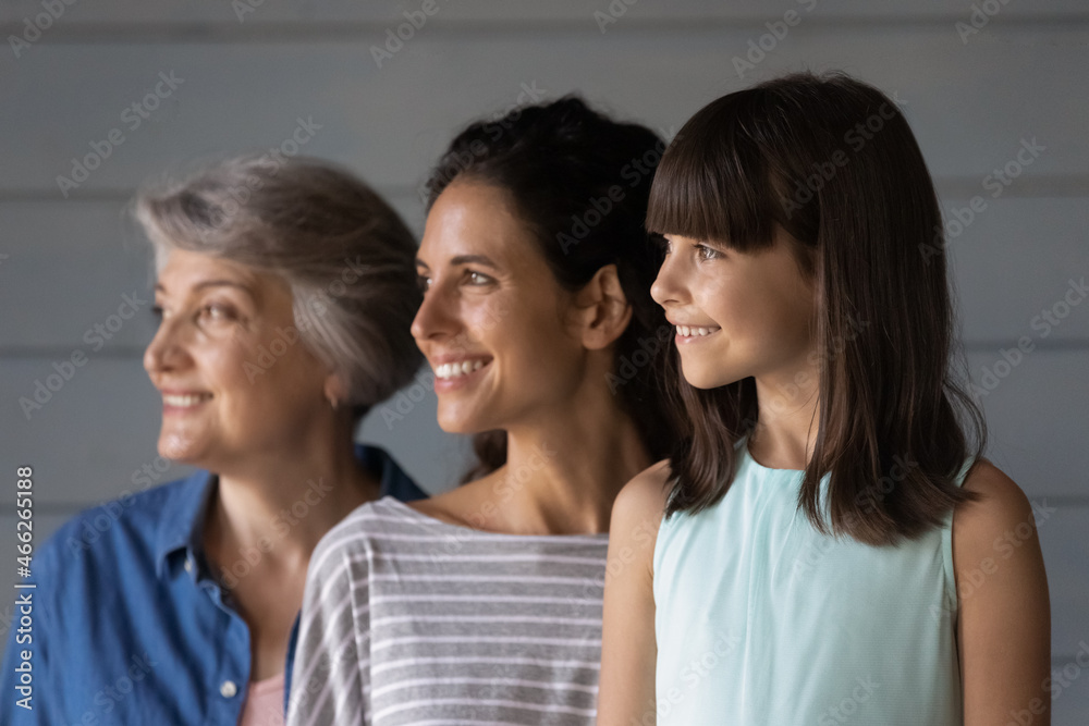 Happy daughter and granddaughter kid posing with mom and grandma, standing in row, looking away, smiling. Three Latin family female generations, 7s girl, young, senior women portrait Happy daughter and granddaughter kid posing with mom and grandma, standing in row, looking away, smiling. Three Latin family female generations, 7s girl, young, senior women portrait