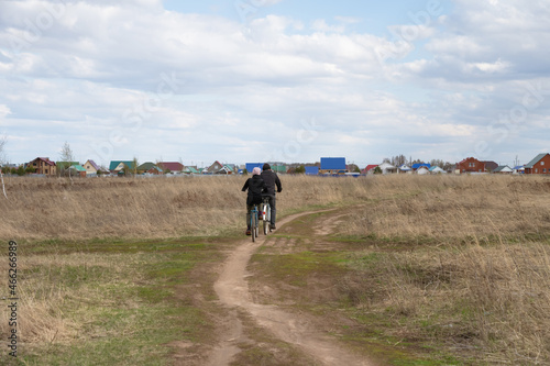 Two cyclists ride a road through a field