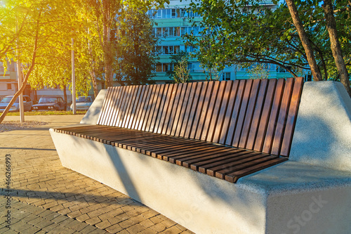 A modern concrete bench covered with brown wooden slats in a city park.