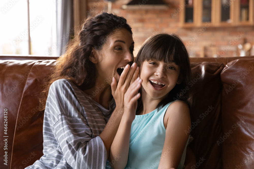 Happy mother and excited daughter kid enjoying friendship, trust, having fun at home. Mom telling secret to joyful girl, whispering in ear, child looking at camera, laughing. Parenthood concept Happy mother and excited daughter kid enjoying friendship, trust, having fun at home. Mom telling secret to joyful girl, whispering in ear, child looking at camera, laughing. Parenthood concept